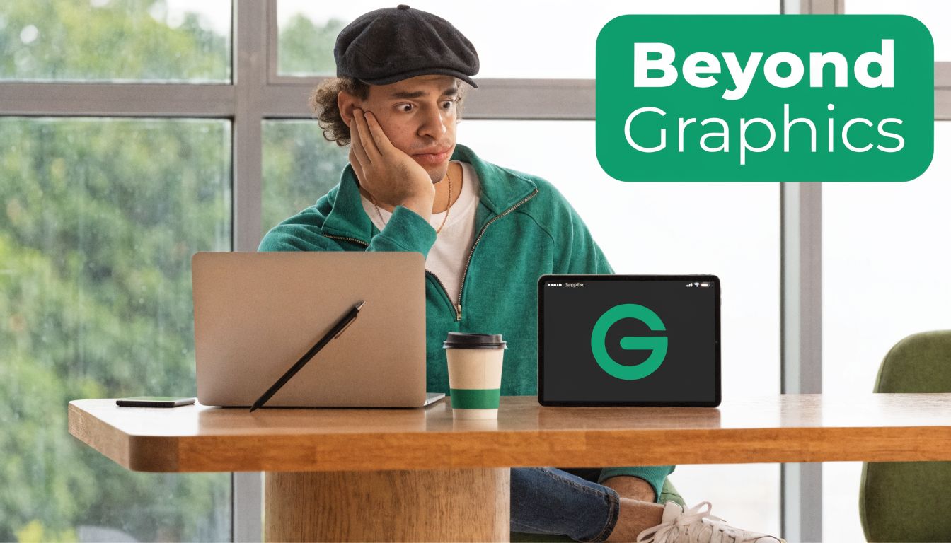 A man wearing a newsboy cap sitting at a desk with a laptop and a tablet displaying a logo.